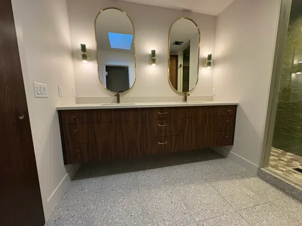 Walnut double bathroom vanity with oval mirrors and a terrazzo floor