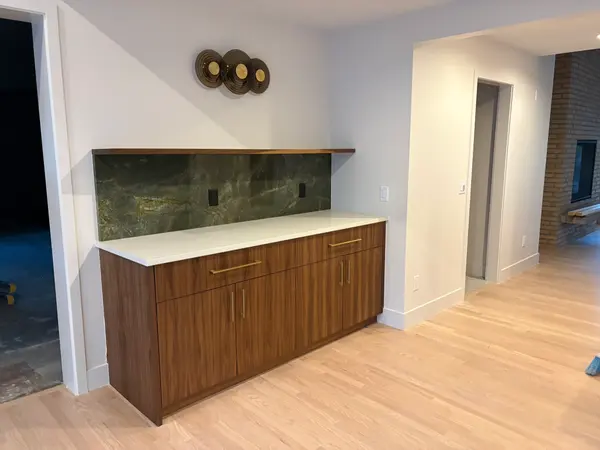 Walnut built-in bar cabinet with a stone slab backsplash and a floating shelf