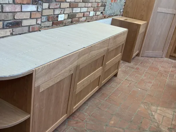 Shaker style cherry kitchen cabinets against an exposed brick wall, countertop still wrapped for protection